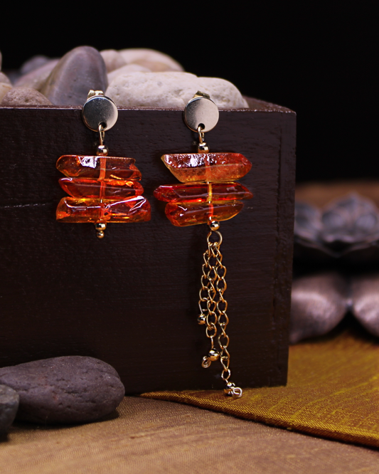 Gold plated stainless steel round stud asymmetrical earrings with orange crystals and dangling gold chain accent. 